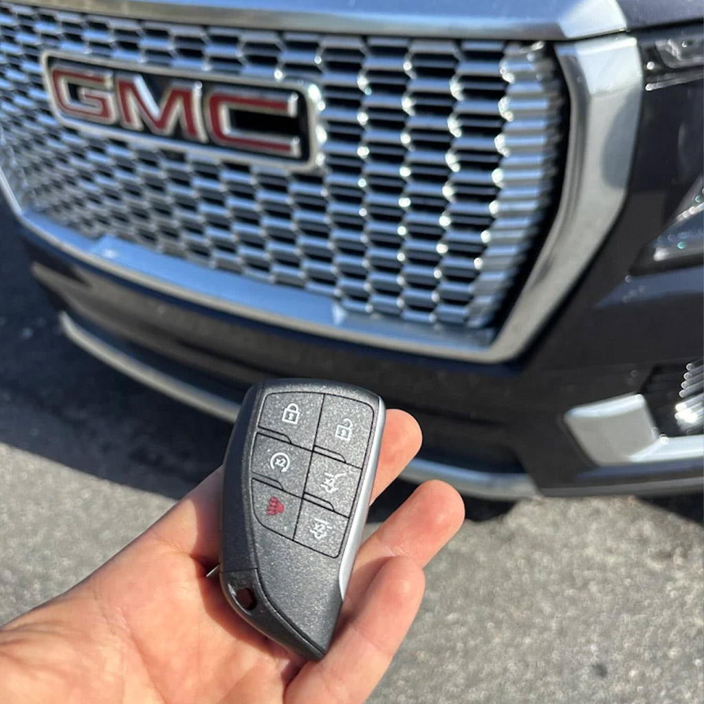 GMC car key replacement service in Panama City Beach with a locksmith holding a new key fob in front of a GMC vehicle